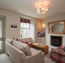 A living room with a beige sofa, a red plaid armchair, a wooden coffee table, a TV on a cabinet, and a fireplace at Swallow's Nest in Windermere