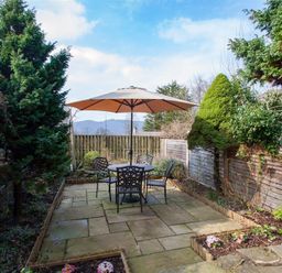 An outdoor patio with a table and four chairs under a large umbrella surrounded by trees and garden beds at Swallow's Nest in Windermere