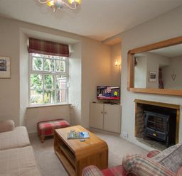 A living room with a sofa armchair wooden coffee table and a television above a cabinet by a window at Swallow's Nest Windermere
