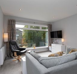 A living room with a large window black chair gray sofa TV on wall and white cabinet at Silver Howe in Grasmere