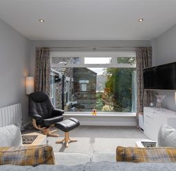 A living room with a large window showing an outside view a black armchair and footstool a gray sofa with cushions a white sideboard a wall-mounted television and table lamps at Silver Howe in Grasmere