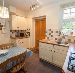 A kitchen with wooden chairs around a table covered with a blue polka dot tablecloth at Briardale Cottage in Ambleside