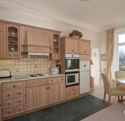 A kitchen with wooden cabinets a stove a refrigerator and a dining table with chairs by a window at Betamere in Ambleside