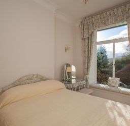 A bedroom with a bed a dressing table and a window seat with floral curtains at Betamere in Ambleside