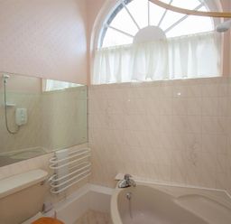 A bathroom with a bathtub shower toilet and a large arched window at Betamere in Ambleside