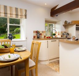 A kitchen and dining area with wooden table set with plates and orange juice and a kitchen counter with sink and appliances at The Hayloft in Ambleside