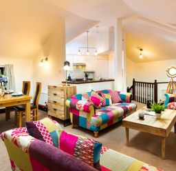 A living room with colorful patchwork sofas a wooden coffee table and a dining table at Falls View Cottage in Ambleside