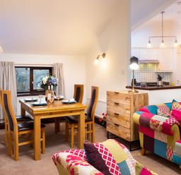 A dining area with a wooden table and chairs next to a sitting area with patchwork upholstered sofas at Falls View Cottage in Ambleside