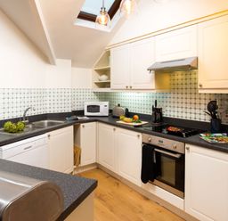 A kitchen with white cabinets black countertops and kitchen appliances at Falls View Cottage in Ambleside