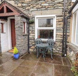 A stone exterior wall with a wooden door under a small roof and a metal table with two chairs outside at Hideaway Cottage in Ambleside