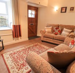 A living room with two sofas a patterned rug a wooden door and a television at Hideaway Cottage in Ambleside
