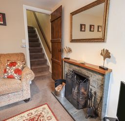 A living room with a patterned sofa cushions a stone fireplace with a firewood holder stairway and a mirror at Hideaway Cottage Ambleside