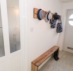 An entryway with a wooden bench black boots under it hats and bags hanging on a wooden wall rack at Bryn Mor in Church Bay