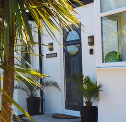 The front entrance of a house with a dark door two potted plants and a window with a decorative object inside at Bryn Mor in Church Bay
