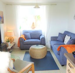 A living room with two blue sofas a wicker coffee table a black stove and a wooden armchair with a white fur throw at Bryn Mor in Church Bay