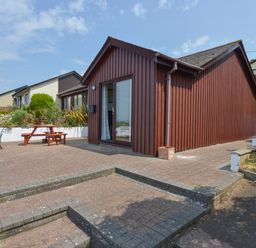 A brown wooden cottage with a patio table and bench seating outside at SoundView in Down Thomas