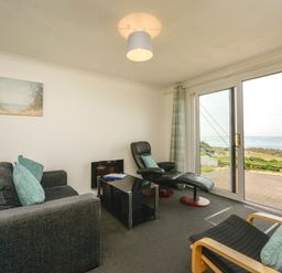 A living room with a sofa armchair recliner glass coffee table and sliding doors opening to a sea view at SoundView in Down Thomas