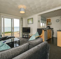 A living room with sofas chairs a television and sliding glass doors leading to a garden and sea view at SoundView in Down Thomas