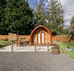 A wooden pod with a patio area and outdoor seating in a fenced garden at Halmore Pod in Halmore near Berkeley