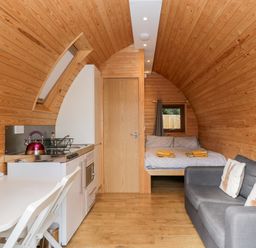 An interior of a wooden pod with a small kitchen area dining table bed and sofa at Halmore Pod in Halmore near Berkeley