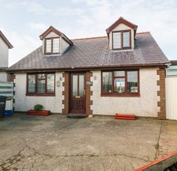 Front view of a two-story house with dormer windows and a paved driveway at Rhiangwyn Cottage in Llanrhyddlad near Cemaes Bay