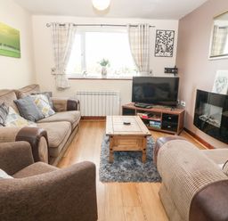 A living room with sofas a wooden coffee table a television and a wall-mounted electric fireplace at Rhiangwyn Cottage in Llanrhyddlad near Cemaes Bay