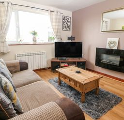 A living room with a sofa wooden coffee table flat screen tv and electric fireplace at Rhiangwyn Cottage in Llanrhyddlad near Cemaes Bay