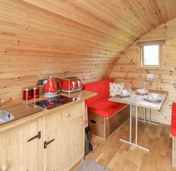 A small wooden kitchen and dining area with red cushions and appliances at Oak View in Llandovery