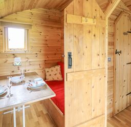 A wooden dining nook with a table set for two and a red cushioned bench at Oak View in Llandovery
