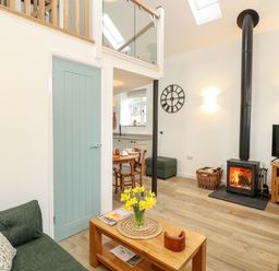 A living room with a green sofa wooden coffee table with flowers and a wood burning stove at Wensum Spring in Horningtoft near Fakenham