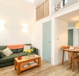 A living area with a green sofa and a wooden coffee table with flowers beside a dining table with chairs at Wensum Spring in Horningtoft near Fakenham