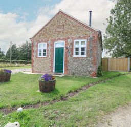 A small stone and brick building with a green door and two windows in a grassy area with flower pots at Wensum Spring Horningtoft near Fakenham
