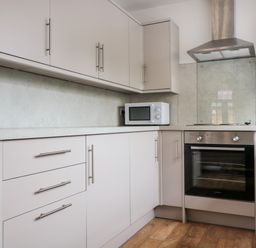A kitchen with white cabinets a built in oven a microwave and a stainless steel extractor hood at Ostlers in Mitcheldean
