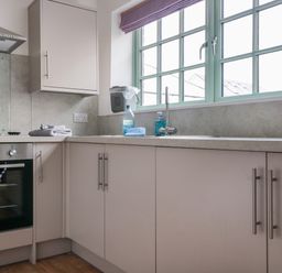A kitchen with built in oven sink and gray cabinets under a green framed window at Ostlers in Mitcheldean