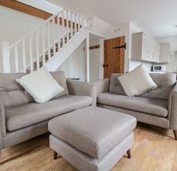 A living area with two sofas a matching ottoman and a staircase in the background at Ostlers in Mitcheldean