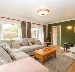 A living room with sofas a wooden coffee table and large windows at The Lodge in Wroxham