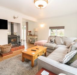 A living room with a gray sofa a wooden coffee table a wood burning stove and a wall mounted tv at The Lodge in Wroxham