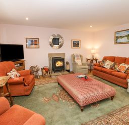 A living room with orange sofas and armchairs a patterned ottoman a fireplace and a television at Todridge Barn in Corbridge