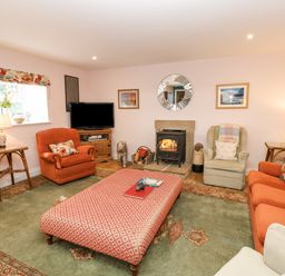 A living room with orange armchairs a patterned ottoman green rug and a fireplace at Todridge Barn in Corbridge
