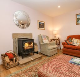 A living room with a wood stove a basket of firewood an armchair an orange sofa and a rug at Todridge Barn in Corbridge
