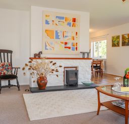 A living room with a white rug wooden rocking chair and a fireplace with artwork above at Goldcrest in Newport Pembrokeshire