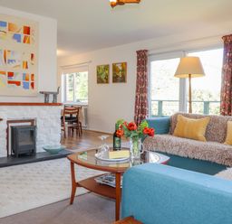 A living room with blue sofas a glass coffee table and a white stone fireplace at Goldcrest in Newport Pembrokeshire