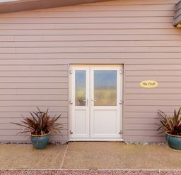 A double white door on a beige exterior wall with two potted plants on each side and a sign that reads The Croft at Leigh Sinton