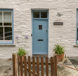 A blue door with two windows and flower pots on a stone patio at Fairfield Cottage in Boscastle