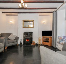 A living room with gray armchairs a wood stove and television at Fairfield Cottage in Boscastle