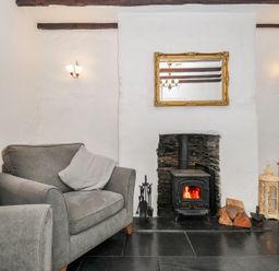 A living room with a fireplace wood stove gray armchairs and a television at Fairfield Cottage in Boscastle