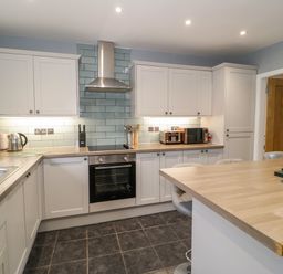 A kitchen with white cabinets wooden countertops an oven stovetop and an island at Big Azzles in Tyn-y-Gongl near Benllech