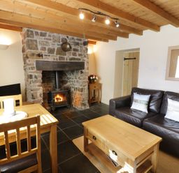 A living room with a stone fireplace wooden coffee table black leather sofa and wooden dining table at Menai Cottage in Brynsiencyn