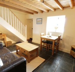 A living room with a leather sofa wooden coffee table dining table with two chairs and a television at Menai Cottage in Brynsiencyn