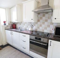 A kitchen with white cabinets a stove oven microwave red pots and a kettle at Menai Cottage in Brynsiencyn
